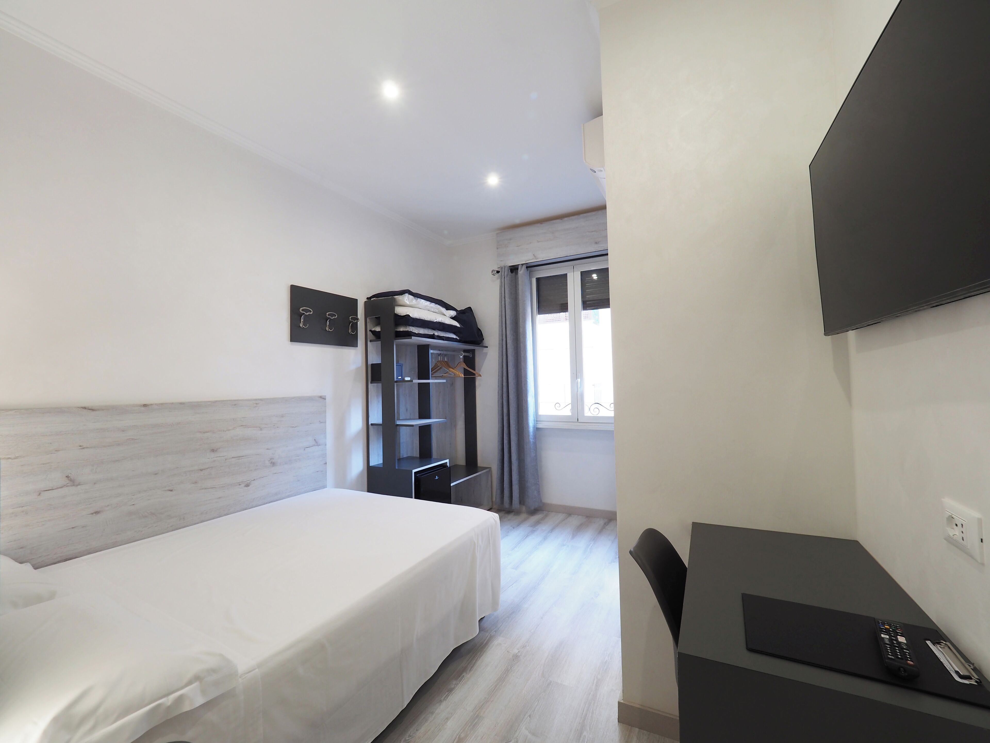 Hotelkamer met een bed, een bureau met stoel, een televisie, een kledingkast en een raam met gordijnen.