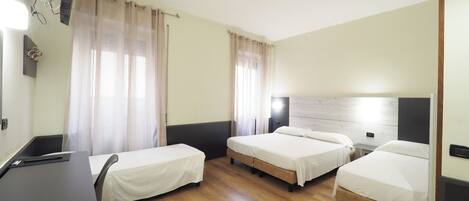 A hotel room with two single beds, a desk, and a flat-screen TV mounted on the wall.