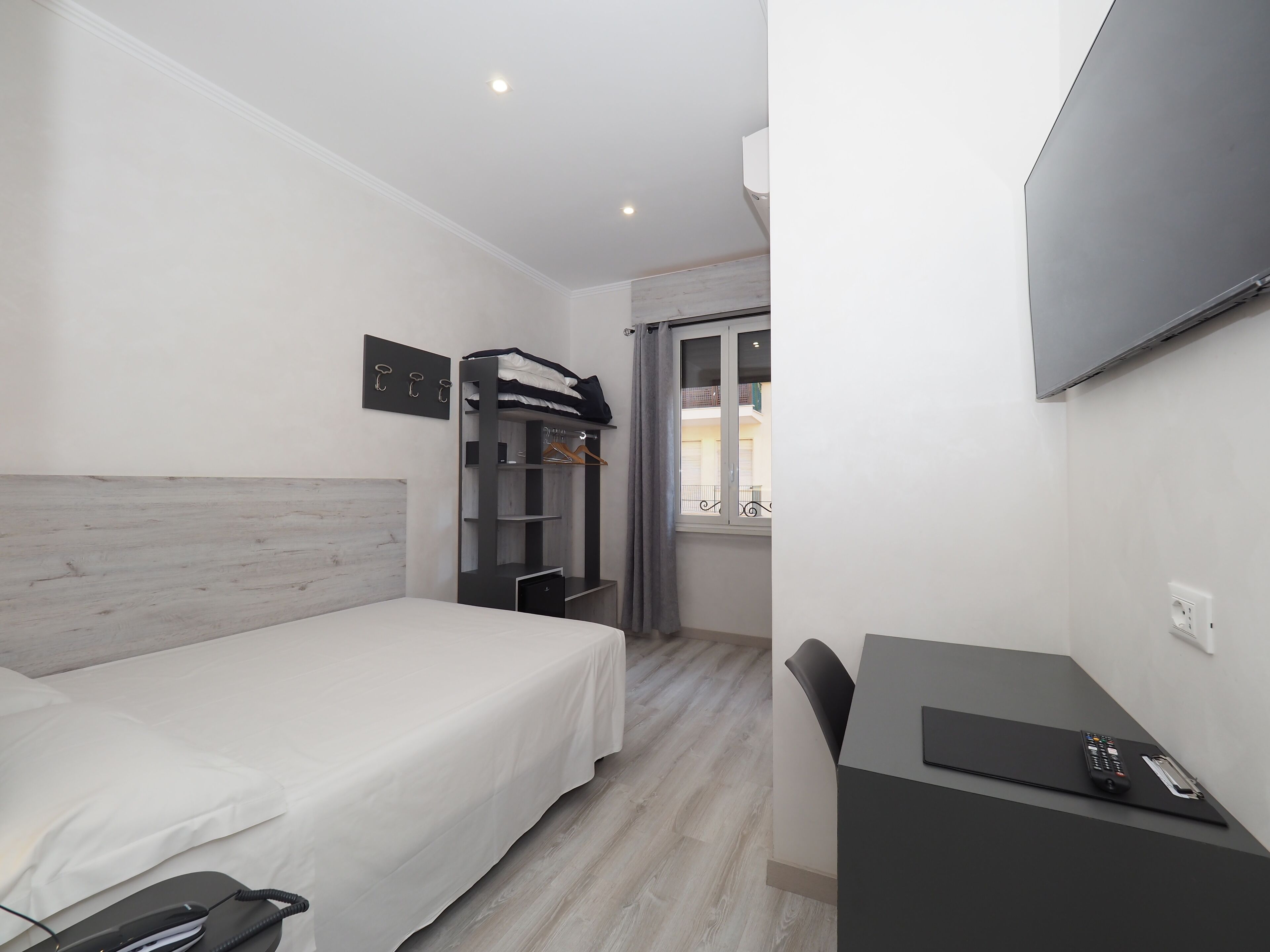 A modern hotel room with a bed, a desk, a wardrobe, and a TV.