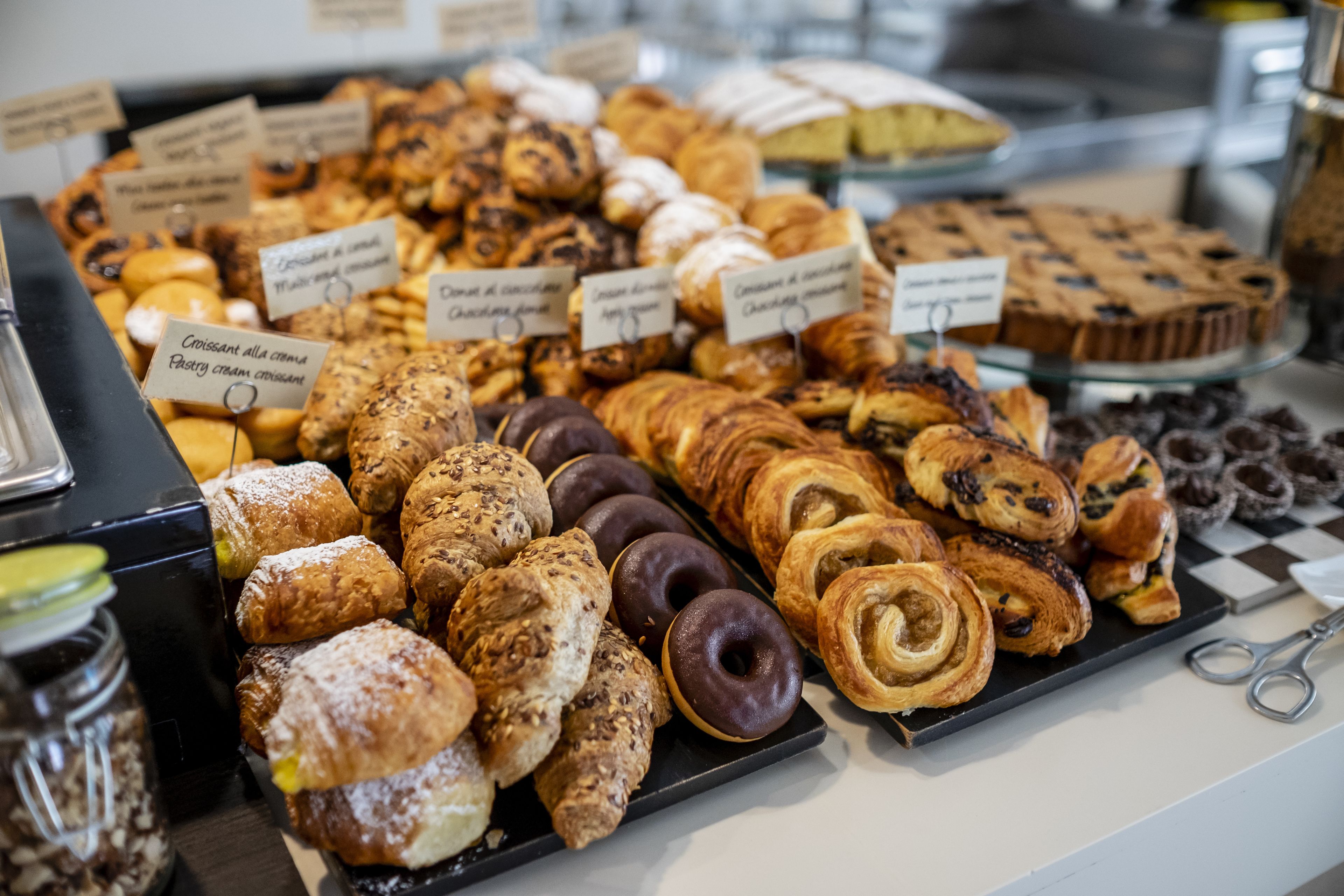 Una exposición de pasteles y productos horneados con etiquetas que indican sus nombres y sabores.