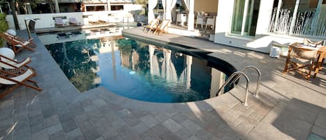 A swimming pool with lounge chairs and a covered seating area.