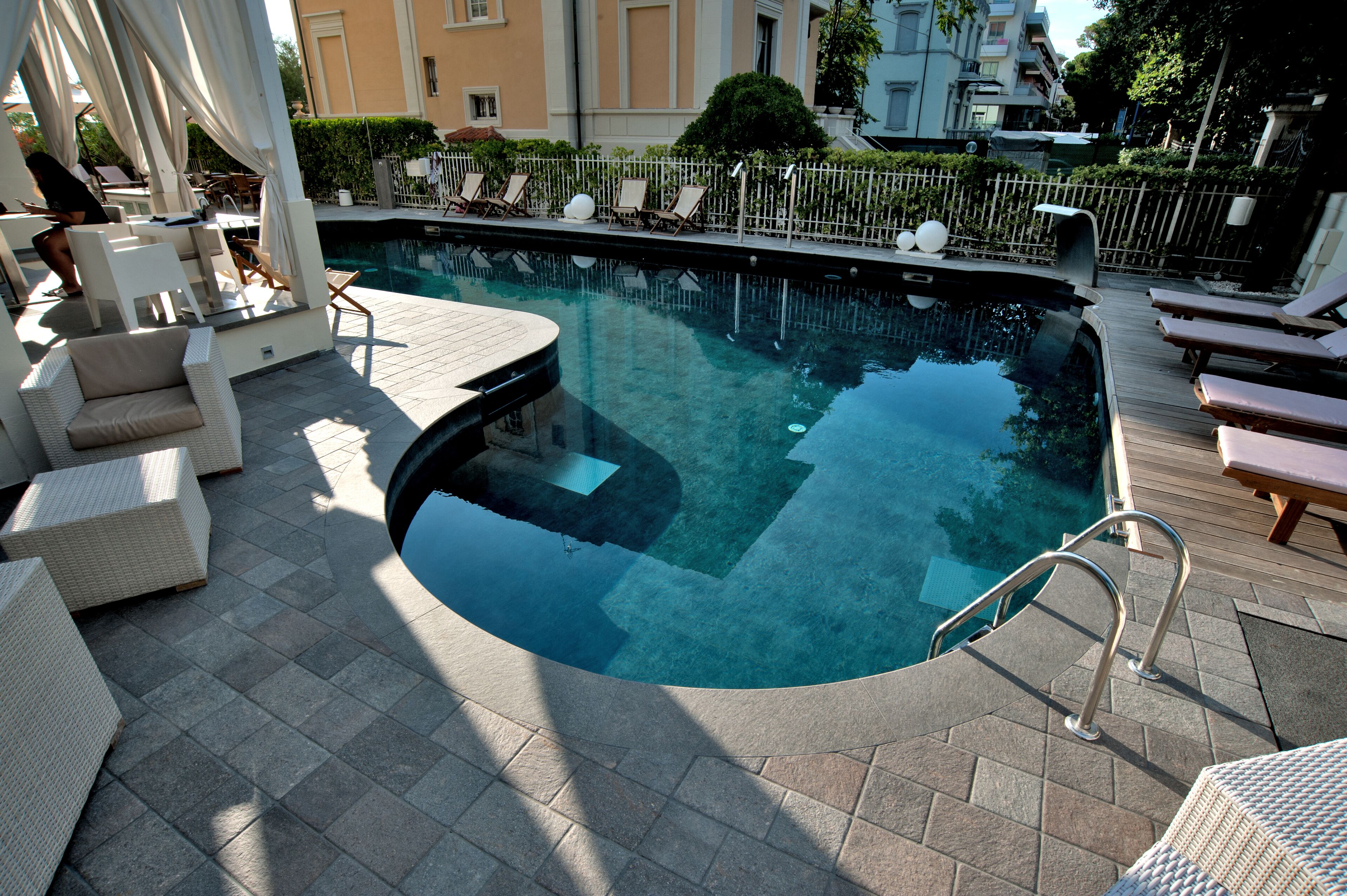 A pool area with lounge chairs, a small table, and a covered seating area.