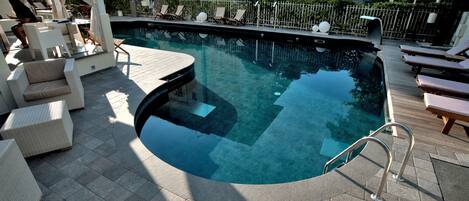 A pool area with lounge chairs, a small table, and a covered seating area.