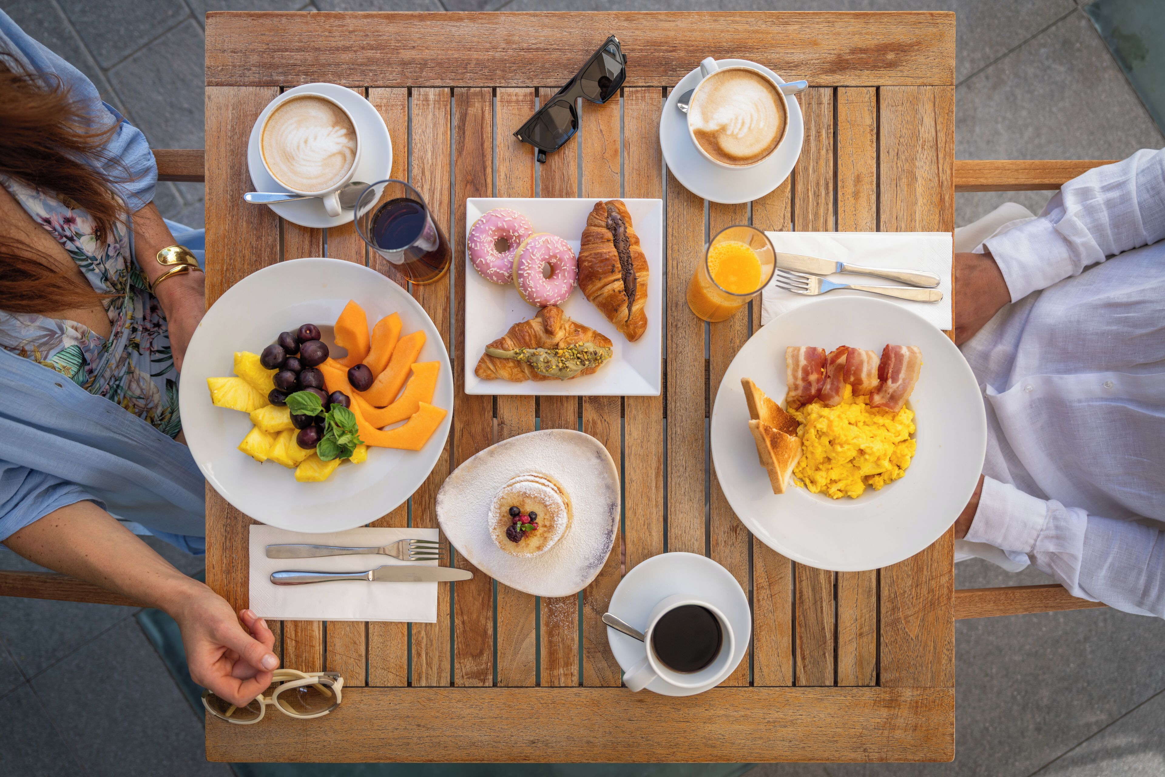 A wooden table with breakfast items including croissants, fruit, and coffee.