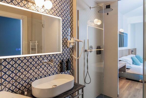 A modern bathroom with a large mirror, a white sink, and a shower with a handheld showerhead. - Le Rose Spa Hotel (Rimini)