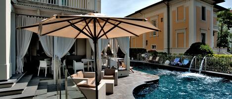 Zona de piscina con sillones de descanso, una sombrilla y una escalera que lleva a un balcón.