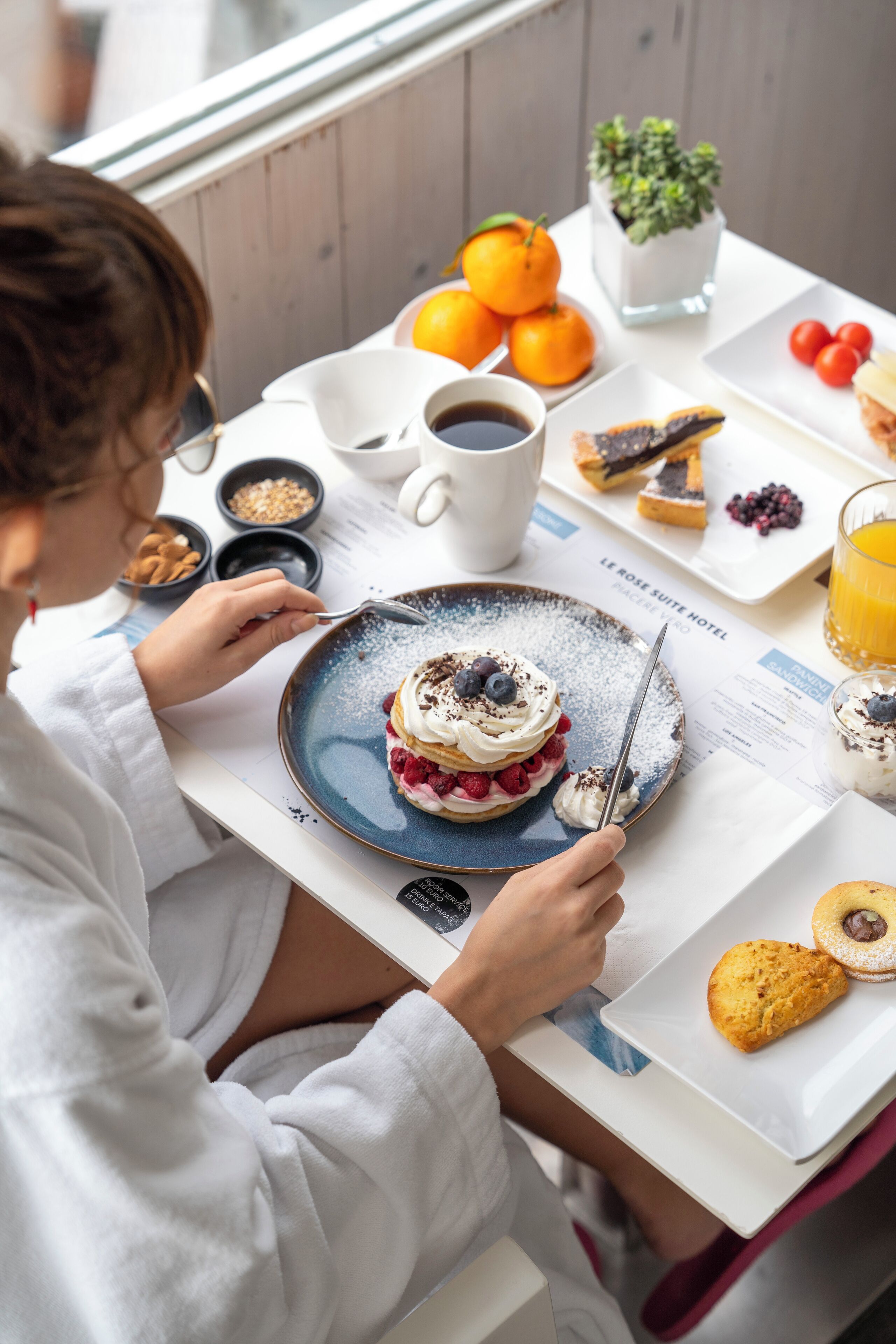 A breakfast setting with a plate of dessert, coffee, and fresh fruit.