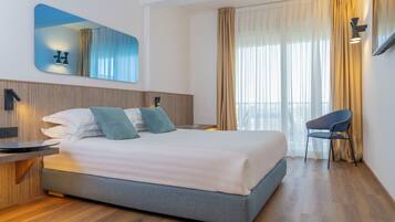 Habitación de hotel moderna con una cama grande, un escritorio, una silla, un espejo y una ventana con cortinas.