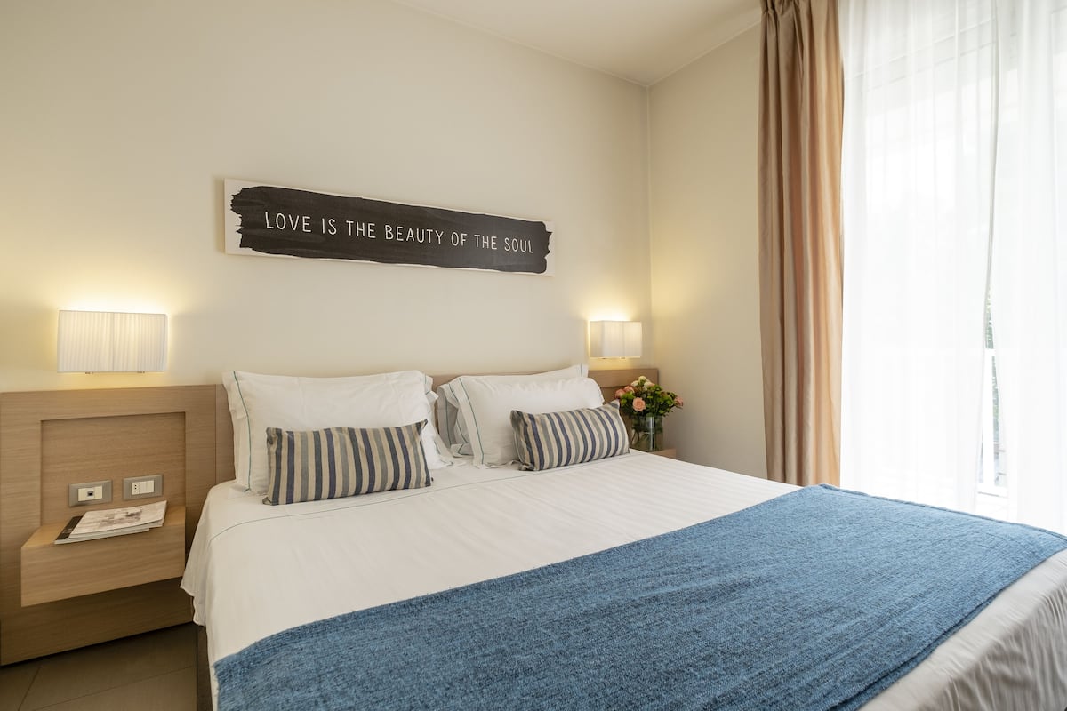 A neatly made bed with a blue blanket, two bedside lamps, a nightstand with a lamp, and a wall sign.