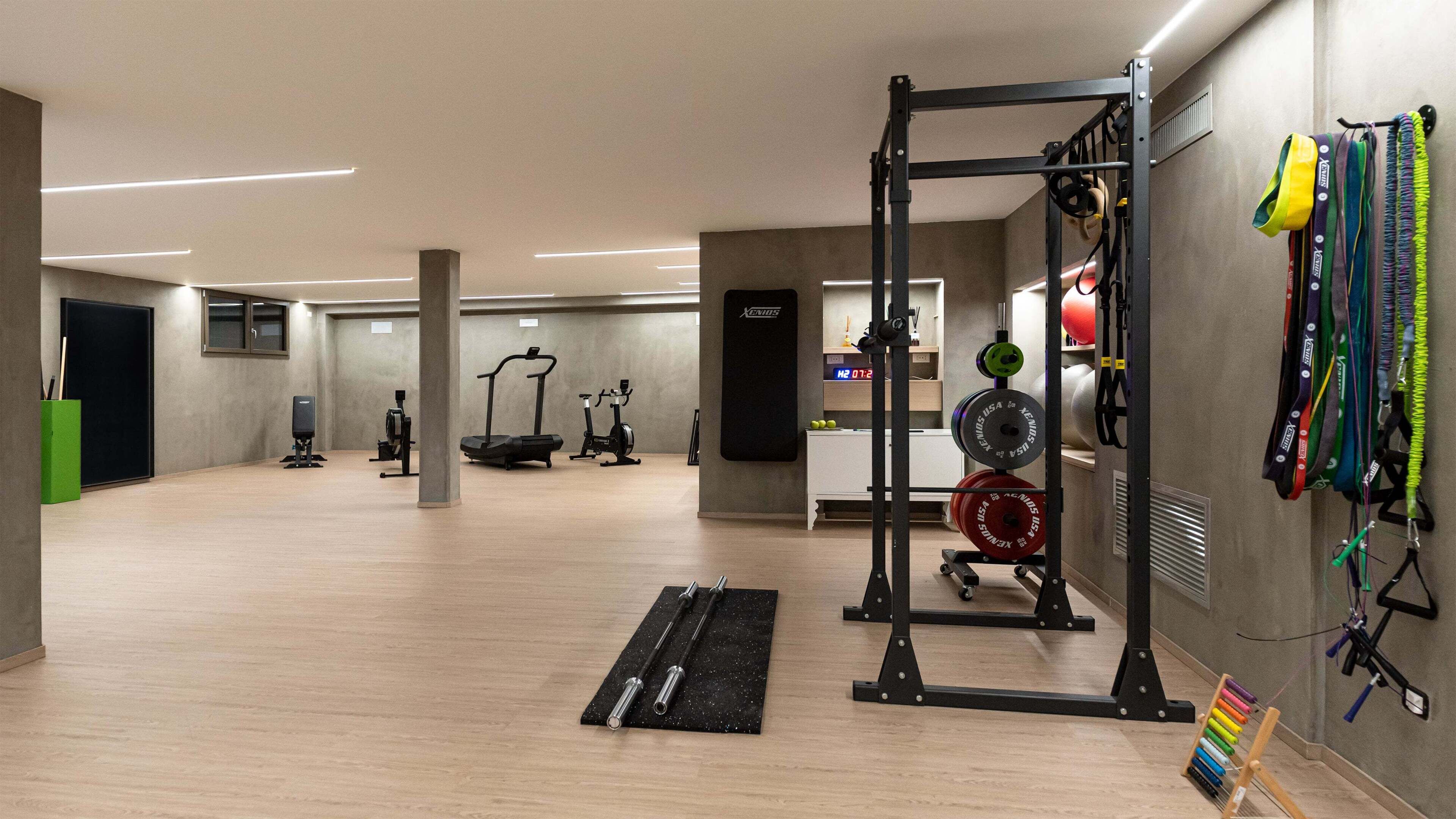 Et fitnesscenter med træningsudstyr, et vægtstativ og en vægmonteret rack med elastikker.