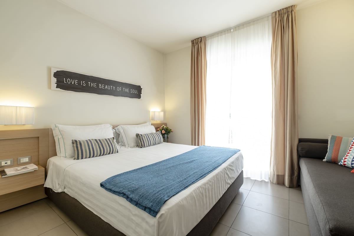A neatly made bed with a blue blanket, a bedside table with a lamp, and a wall sign that reads "LOVE IS THE BEAUTY OF THE SOUL".