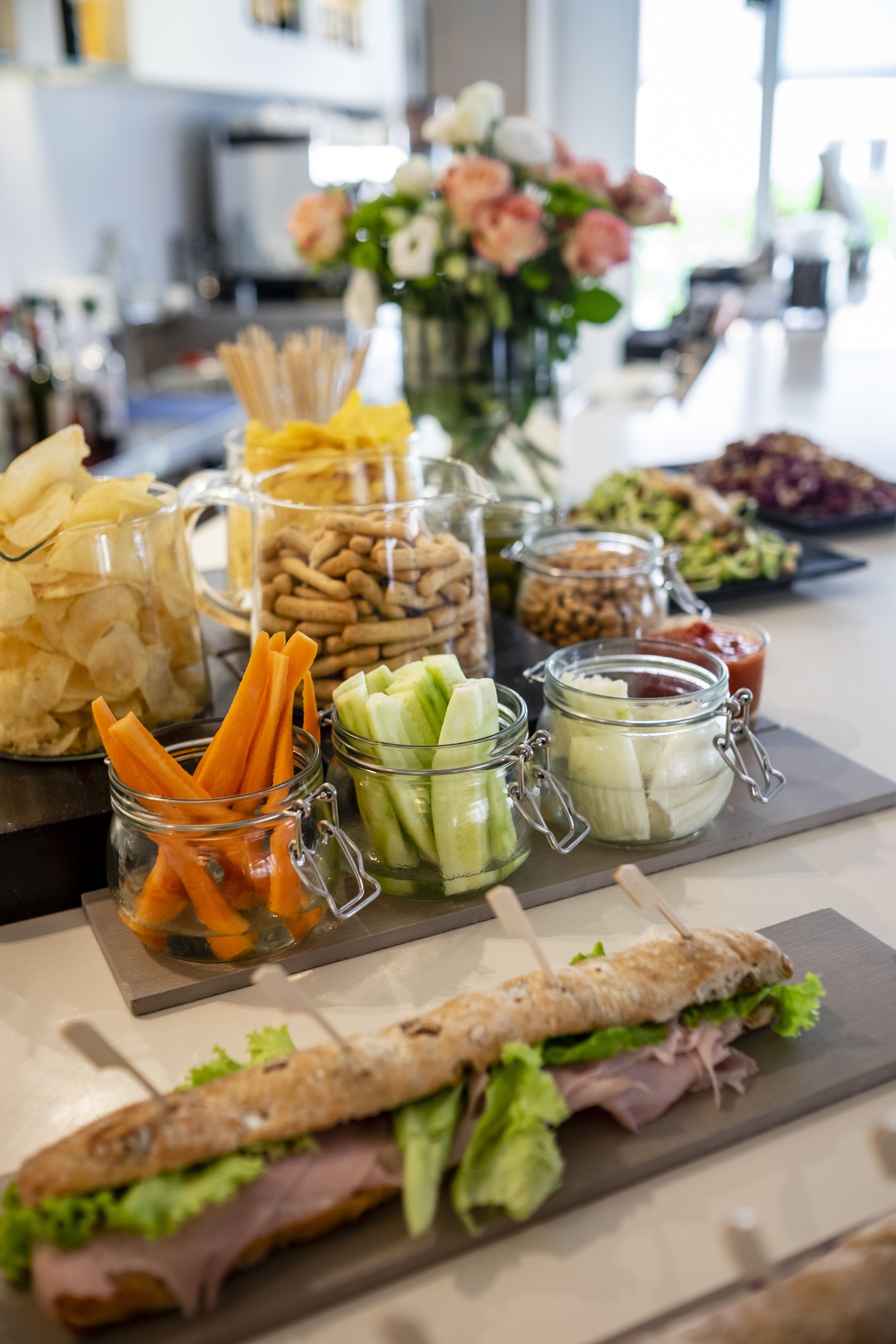 A buffet table with various food items including chips, carrots, celery, and a sandwich.