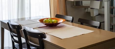 A dining area with a wooden table, black chairs, a bowl of fruit, and a staircase in the background.