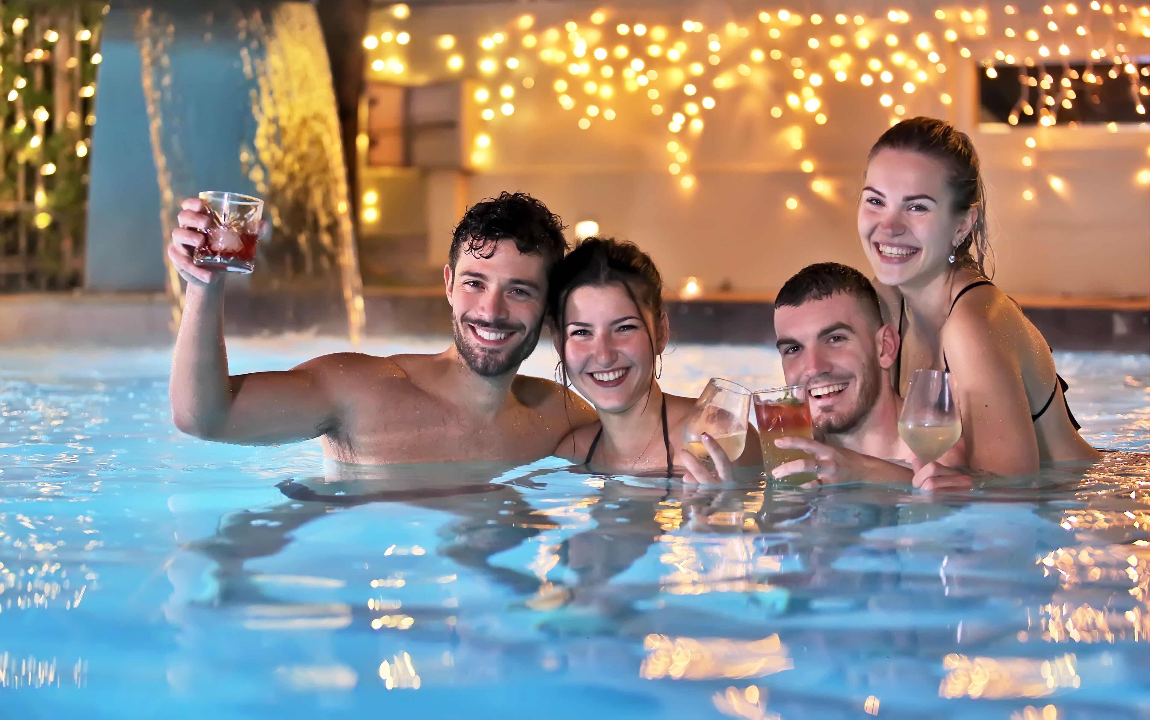 Um grupo de pessoas em uma piscina, com luzes de corda ao fundo.