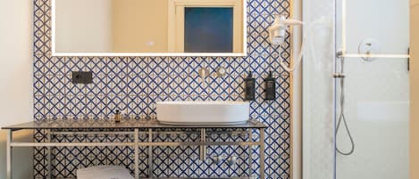 Un baño con un lavamanos blanco, un espejo, un perchero para toallas y una ducha.