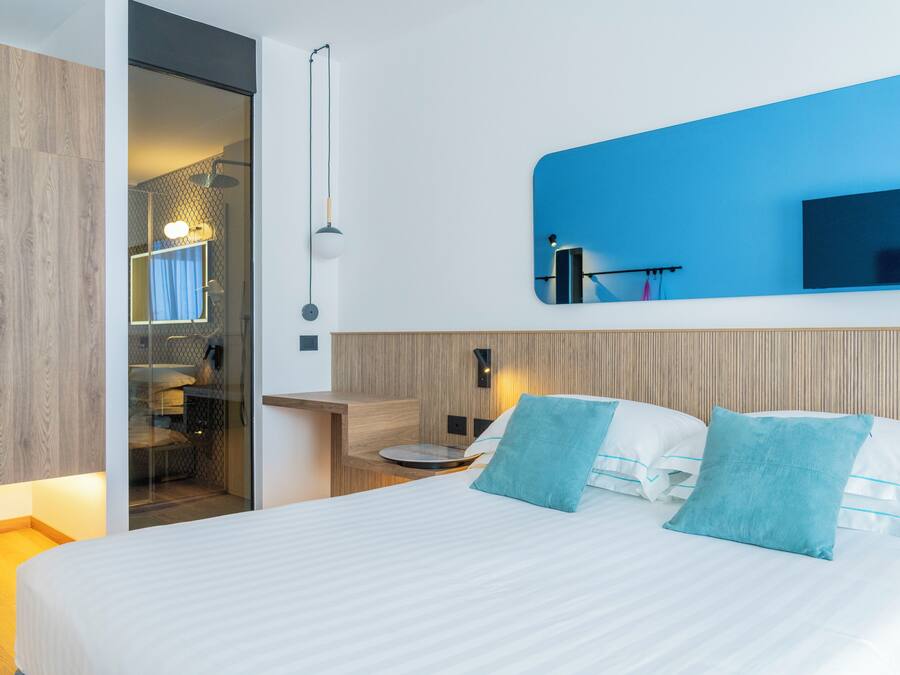 A modern hotel room with a bed, a TV, a desk, and a shower area.