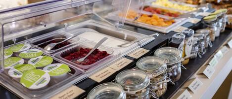 Un bufé con diversos alimentos y condimentos, incluyendo recipientes etiquetados con yogur y salsas.
