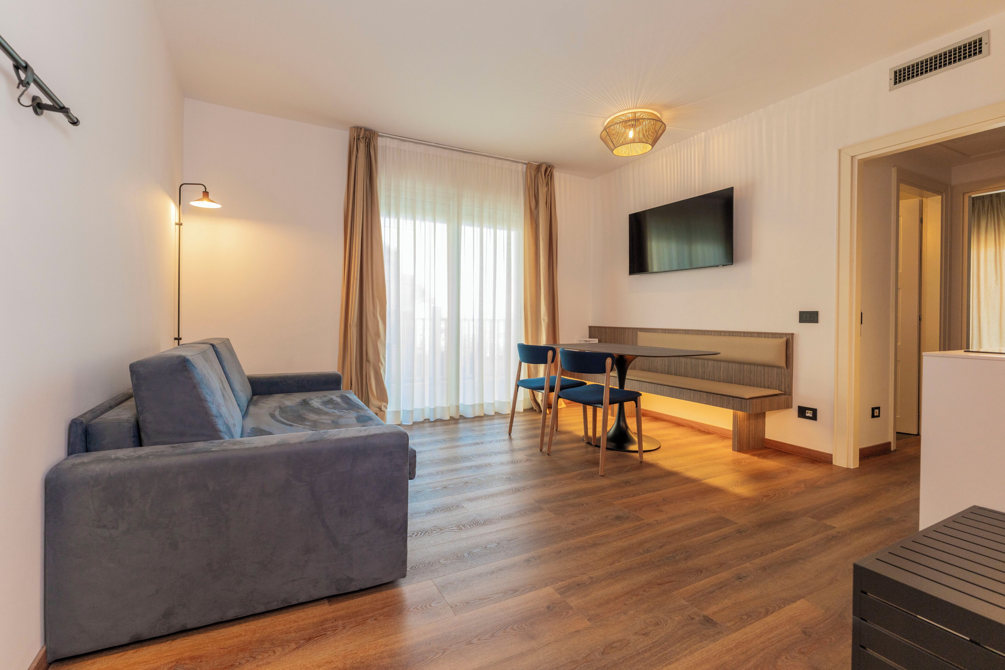 Una sala moderna con sofá, una mesa de comedor con sillas, un televisor de pantalla plana montado en la pared y piso de madera.