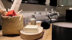 A bathroom with a woven basket containing toiletries, a soap bar, a bottle, and a black object on a round wooden tray.