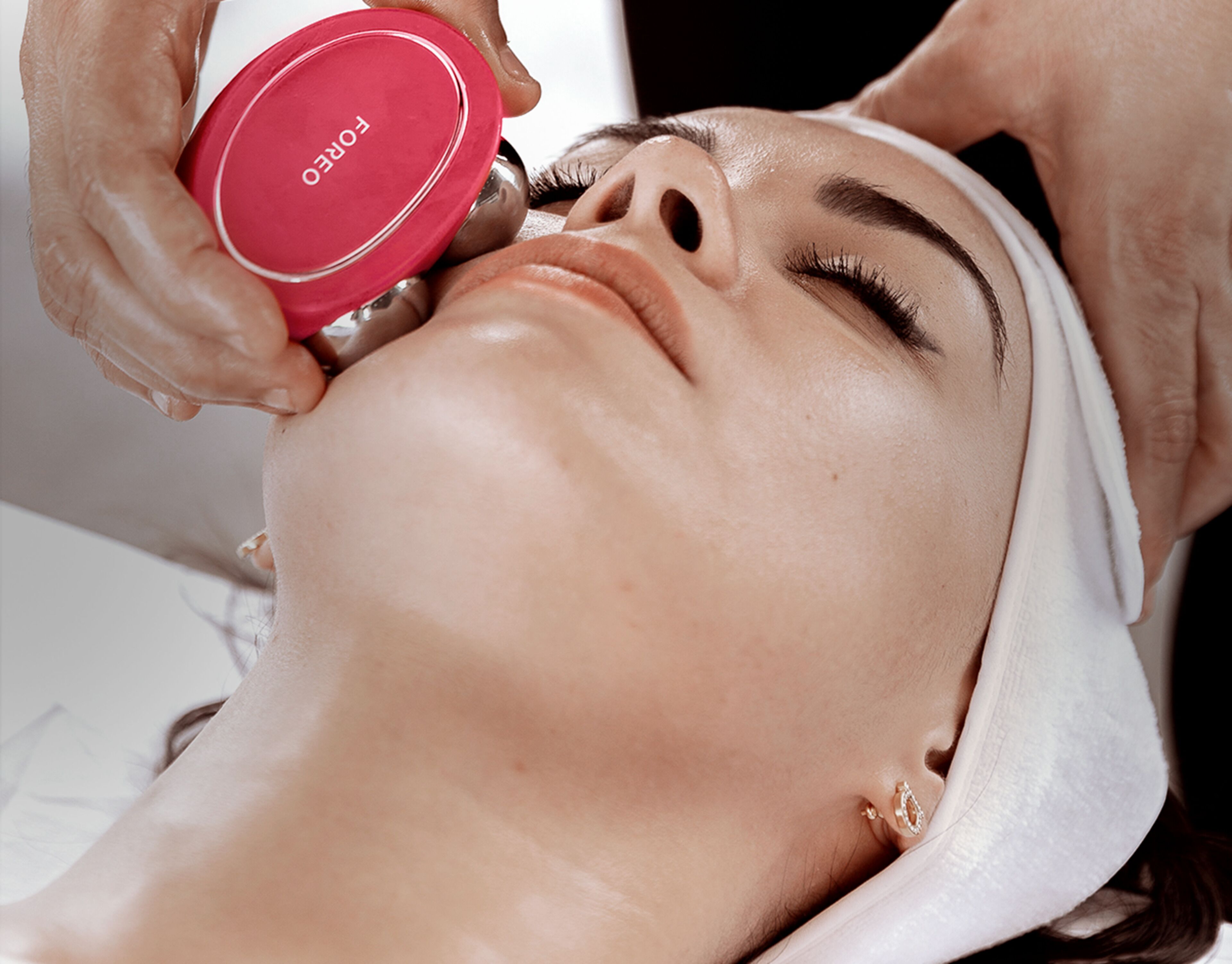 A person lying down with a red container labeled 'FOREO' being used on their face.