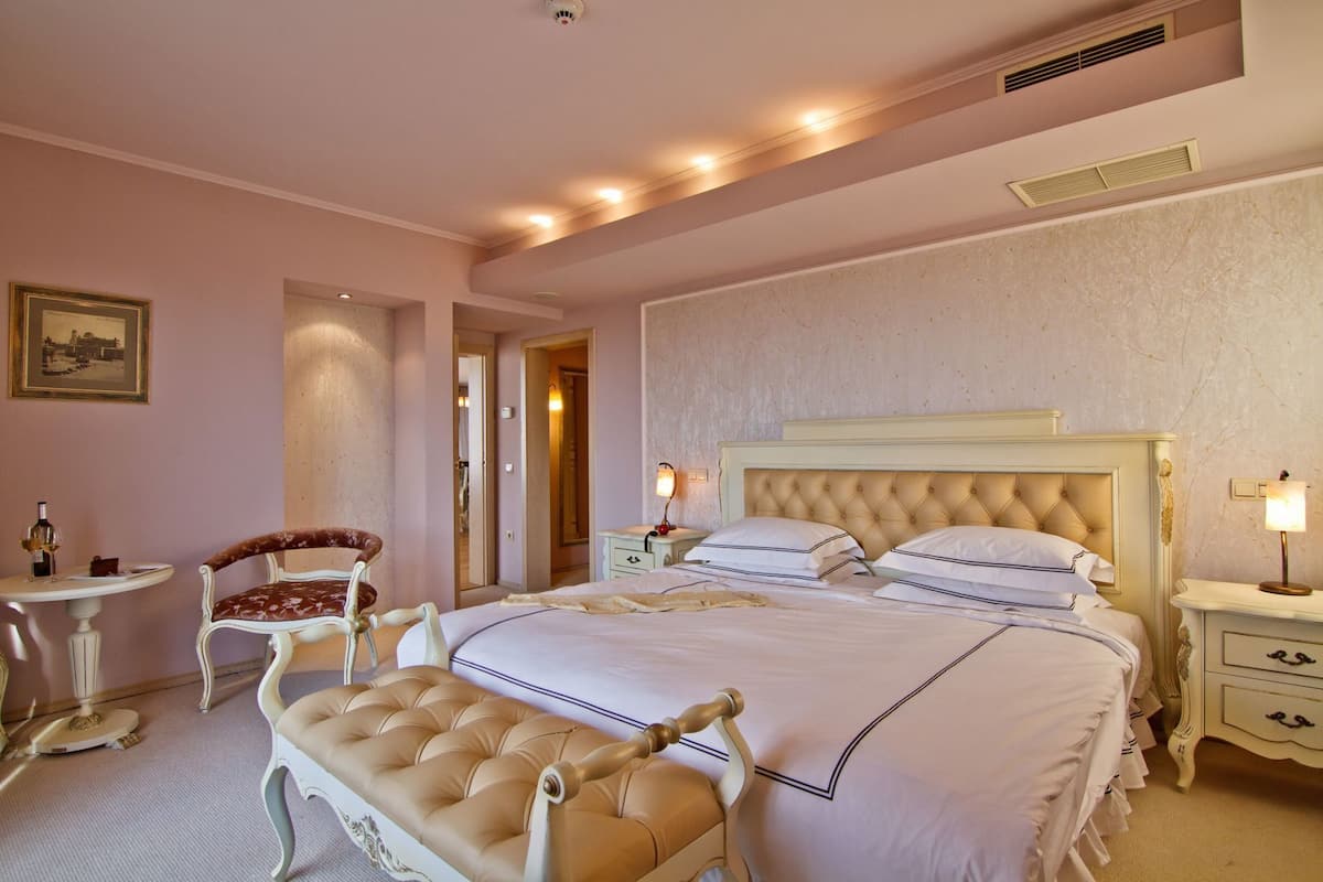 A hotel room with a large bed, a chair, a bedside table, a lamp, and a picture on the wall.