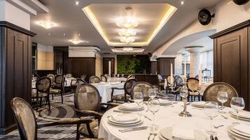 A formal dining room with round tables, chairs, and chandeliers.