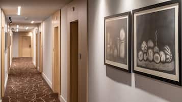 Un couloir d’hôtel avec un tapis à motifs, des portes en bois et deux œuvres d’art encadrées accrochées au mur.