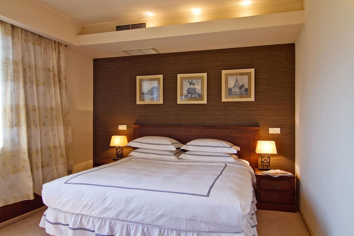 A hotel room with a large bed, two bedside lamps, a headboard with a dark wood finish, and three framed pictures on the wall.