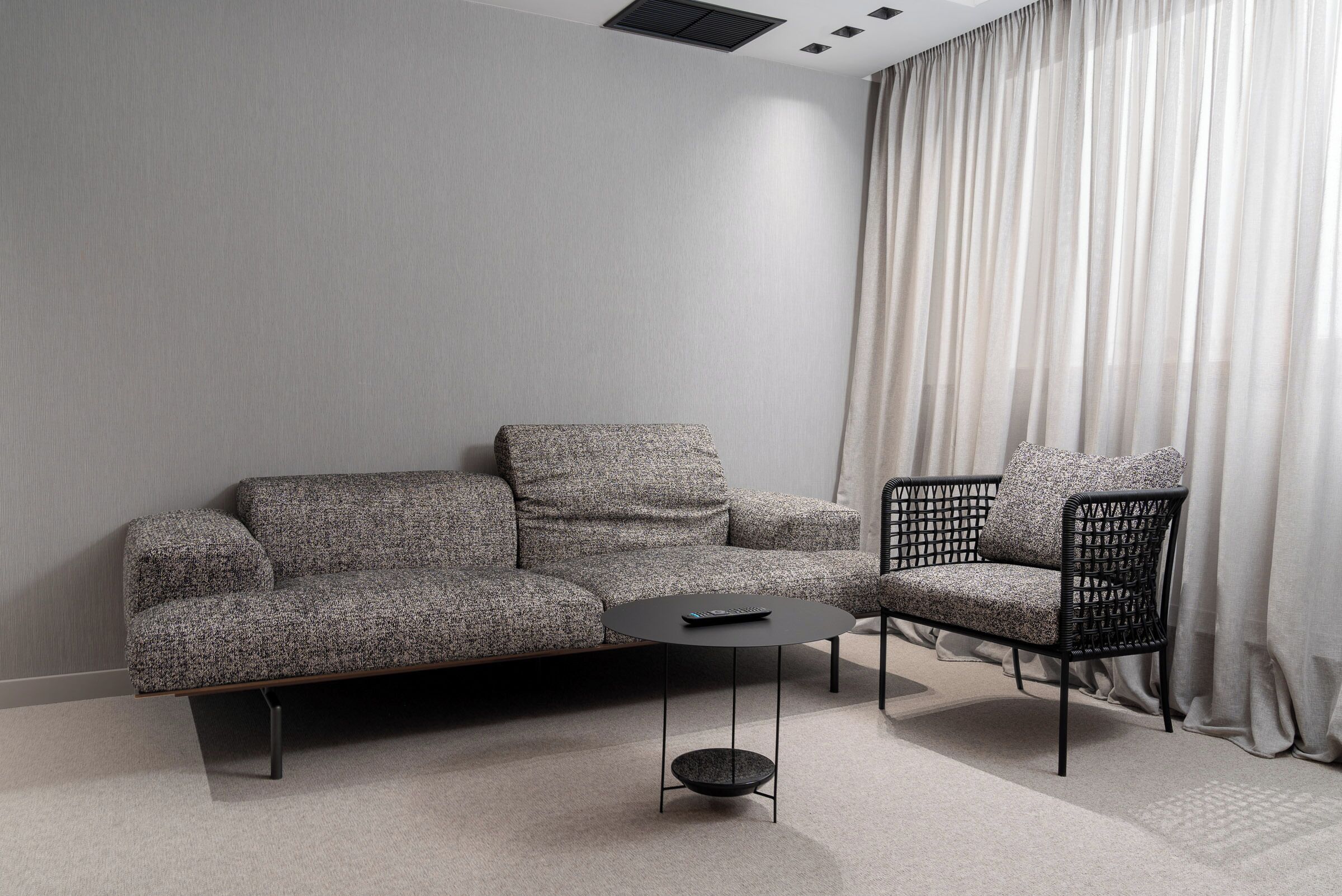 Una sala de estar moderna con un sofá gris, una mesa de centro negra y una silla de mimbre negro.