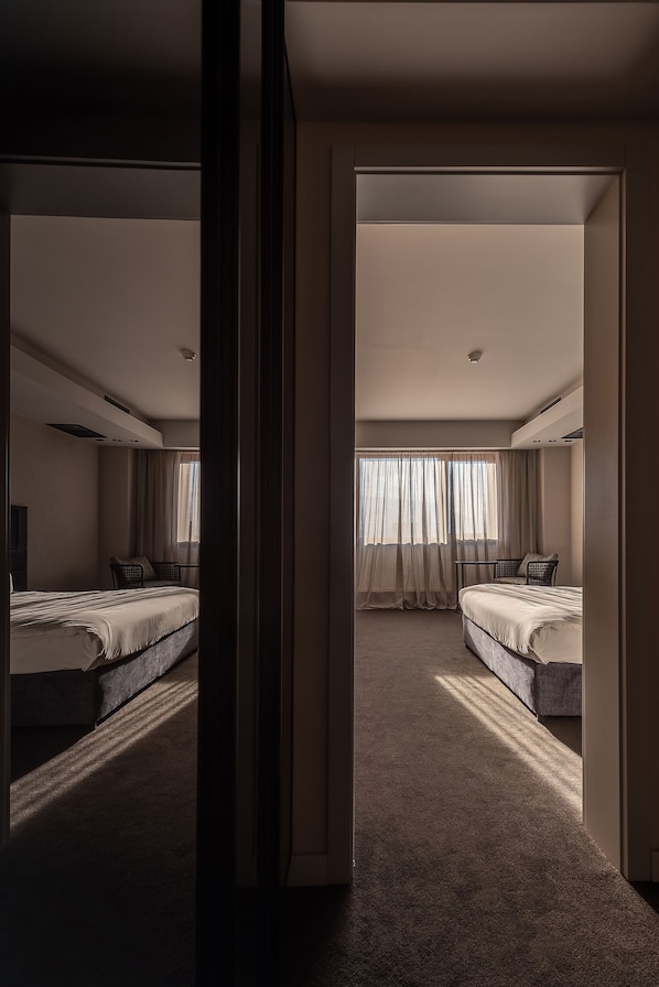 Habitación de hotel con dos camas, un ventanal con cortinas, piso alfombrado e iluminación empotrada en el techo.