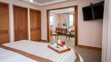 Habitación de hotel con una cama grande, una bandeja con alimentos para el desayuno, un televisor y vista al comedor.