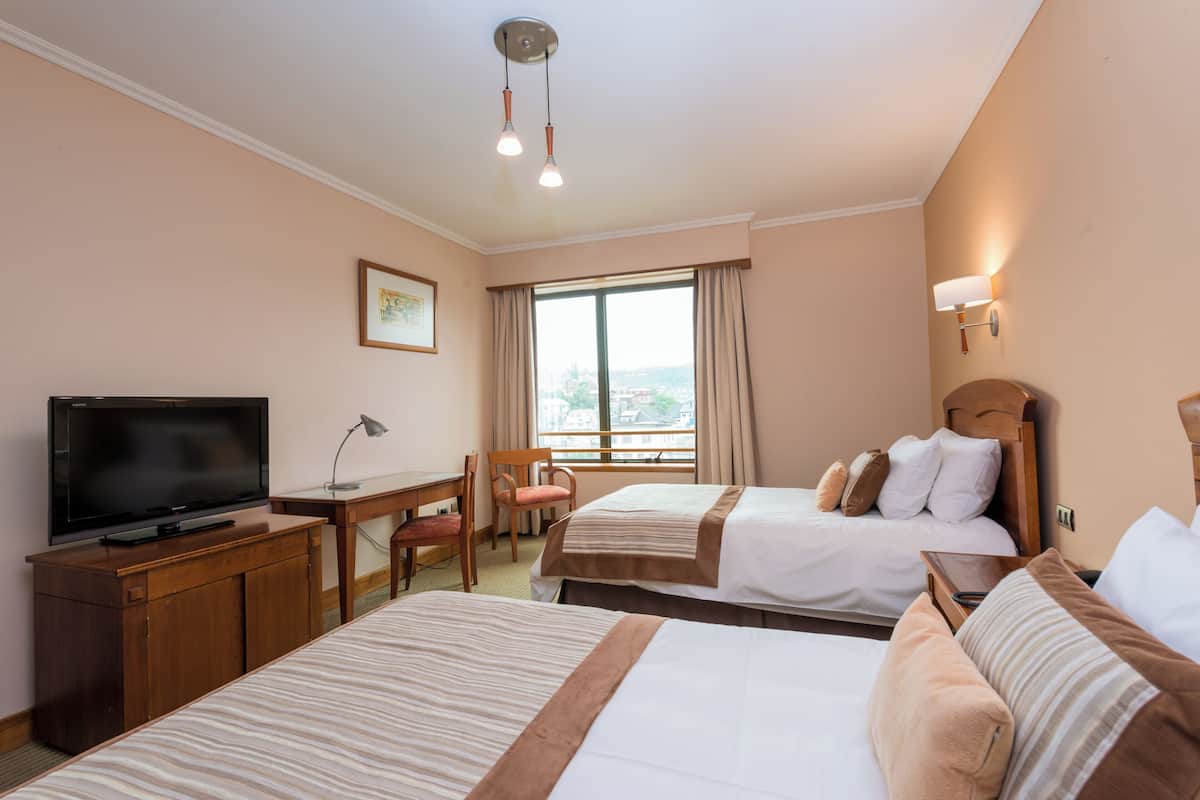 Habitación de hotel con dos camas, un escritorio con silla, televisor y ventana con cortinas.