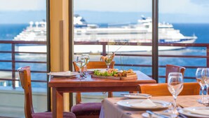 Mesa servida con platos, vasos y un aperitivo de mariscos, con vista a un crucero en el agua.