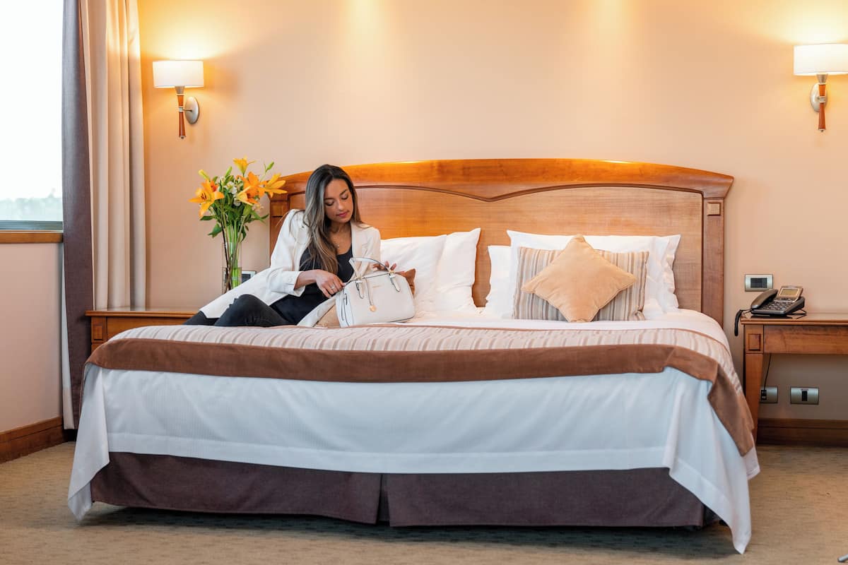 Una cama bien hecha con cabecera de madera, una mesita de noche con lámpara y un teléfono.