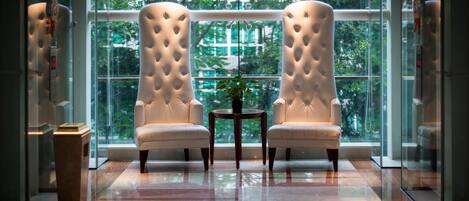 A room with two tufted armchairs facing a large window with a view of greenery.