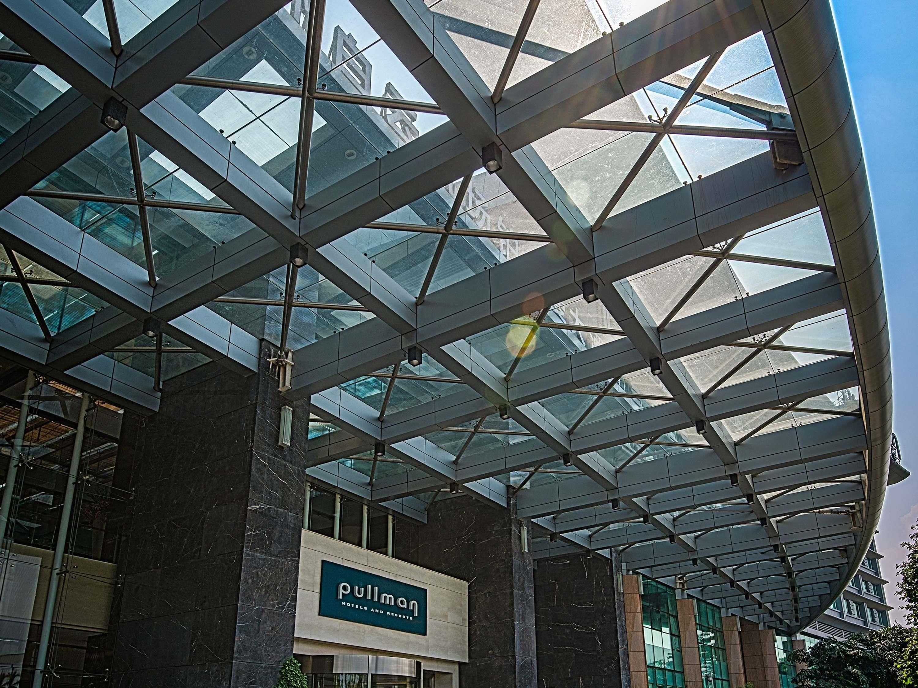 A hotel with a modern glass and steel structure, a sign for Pullman Hotels and Resorts, and a view of the cityscape through the glass.