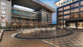 Un hotel dal design architettonico moderno, con un cortile centrale arredato da tavoli e sedie, circondato da edifici con ampie vetrate e un cartello luminoso dell'hotel.
