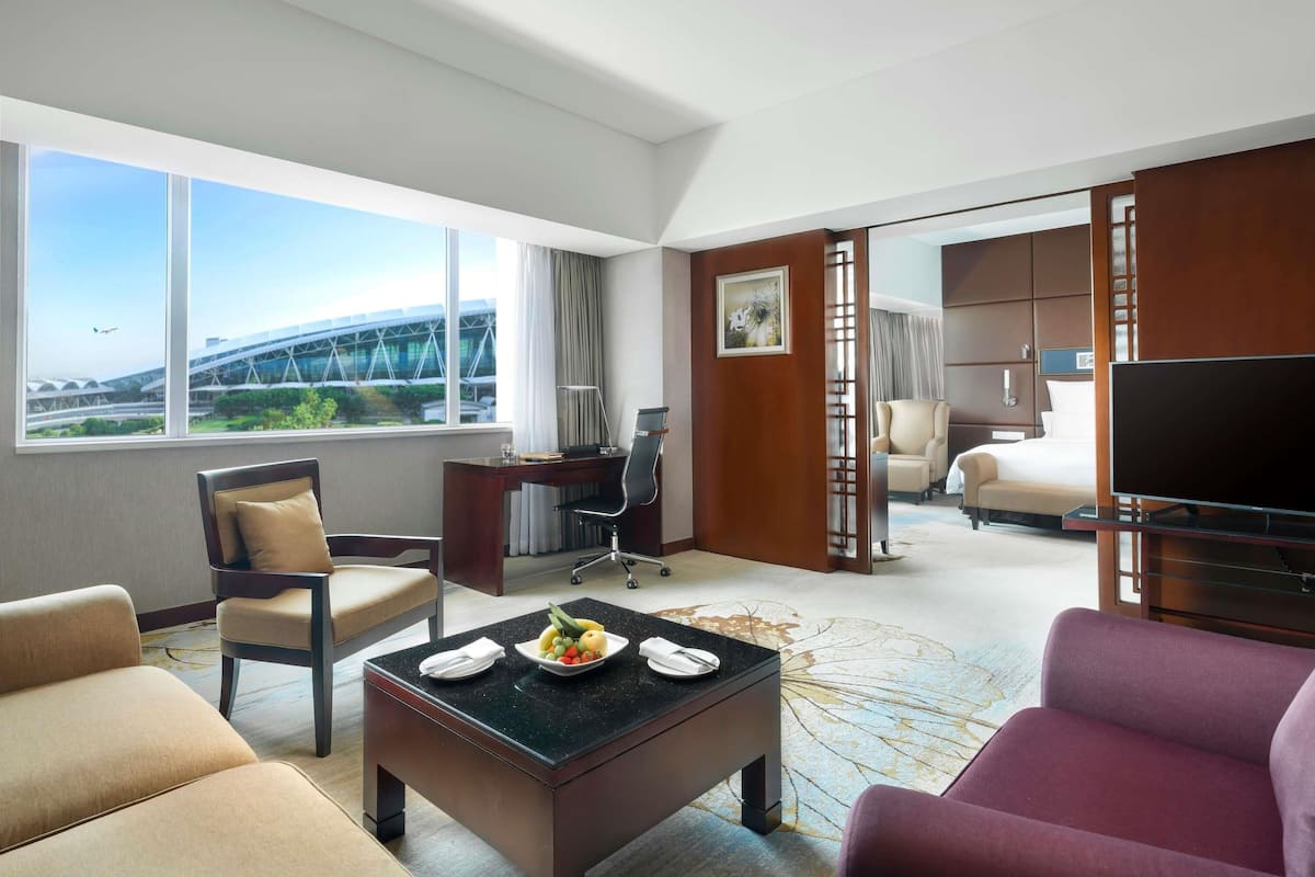 A hotel room with a desk, chairs, a flat-screen TV, a bed, and a view of a bridge.