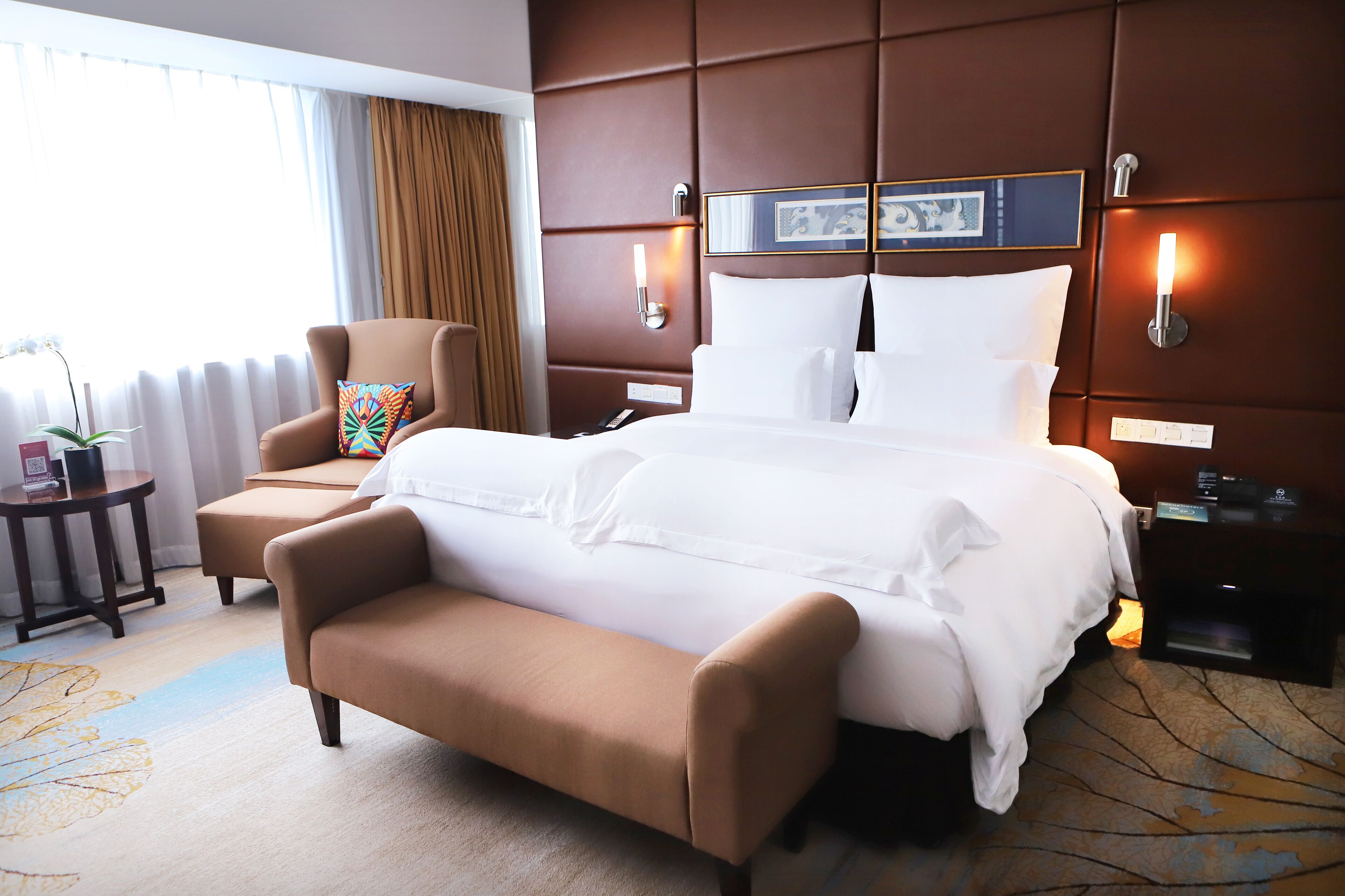 A hotel room with a large bed, a chair, a bedside table, and a lamp.