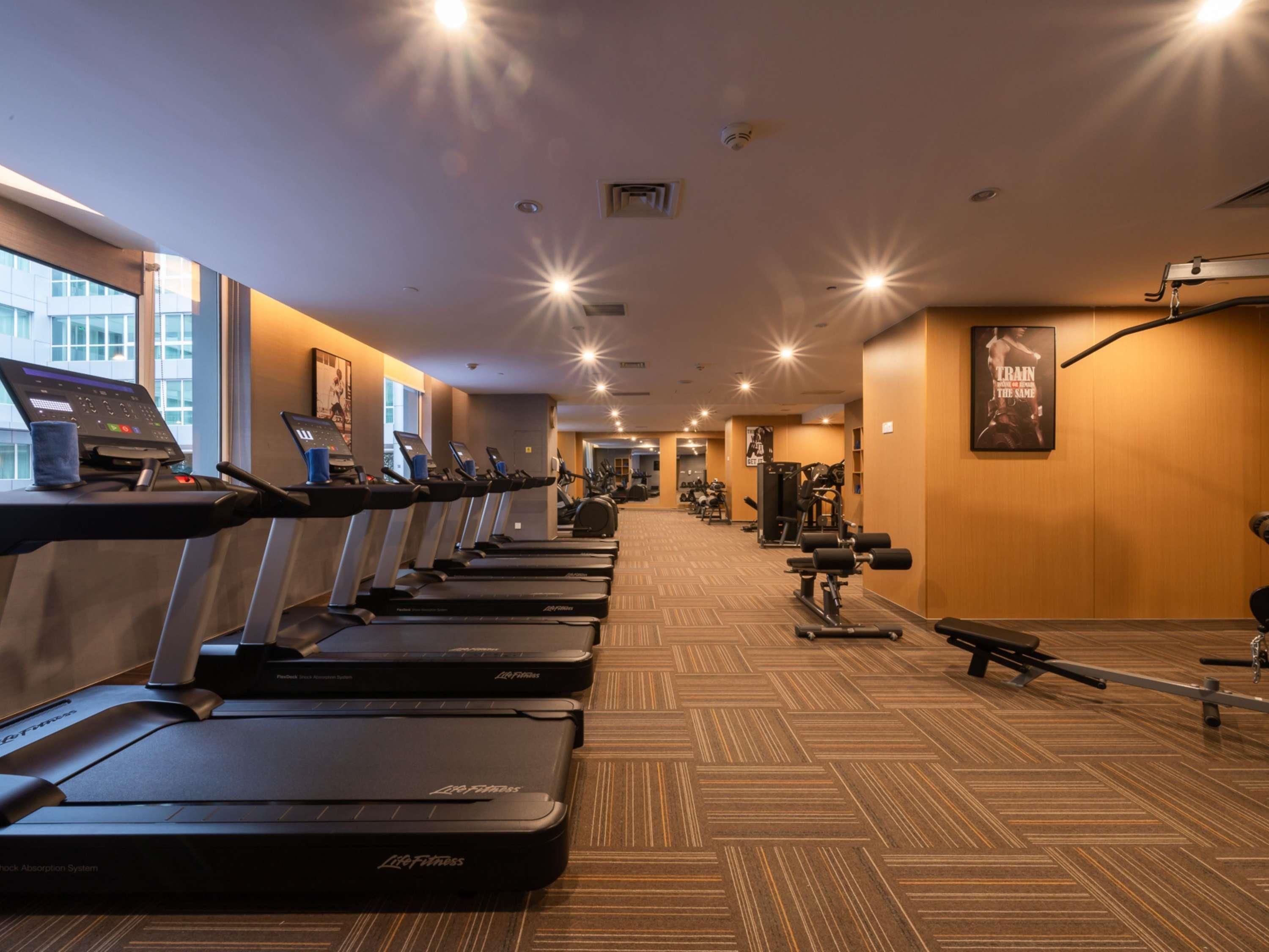 Een fitnessruimte met loopbanden, krachtapparaten en een visgraatvloer.