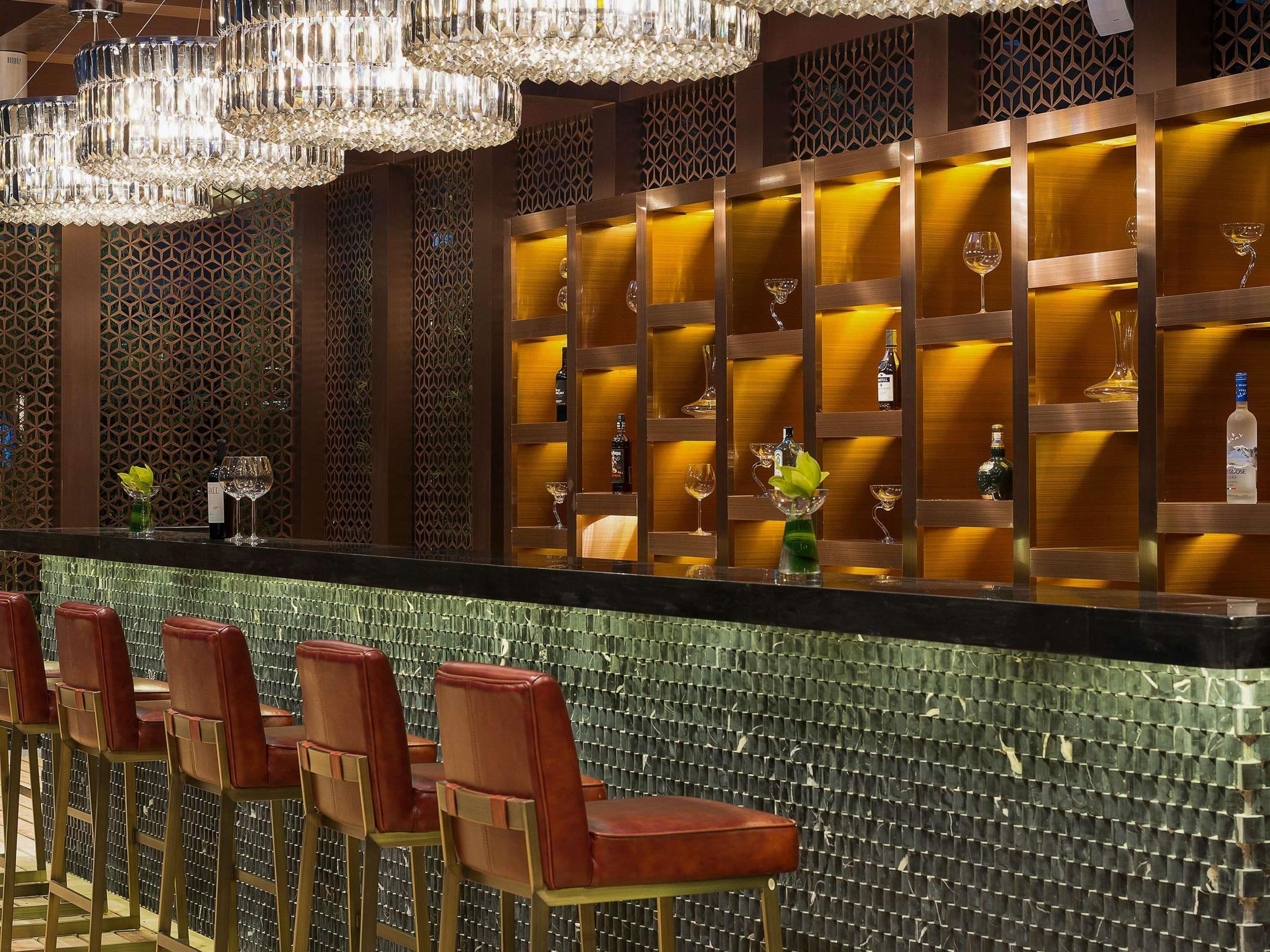 A bar area with a patterned wall, a counter with stools, and decorative lighting.