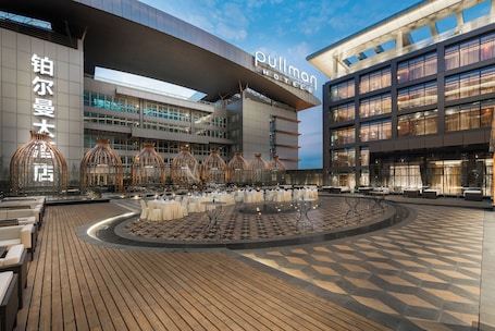 A hotel with a modern design, featuring a spacious outdoor area with tables and chairs, a central fountain, and a large building with signage.