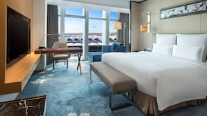 Habitación de hotel con una cama grande, un escritorio con una computadora portátil, una silla y vistas al aeropuerto.