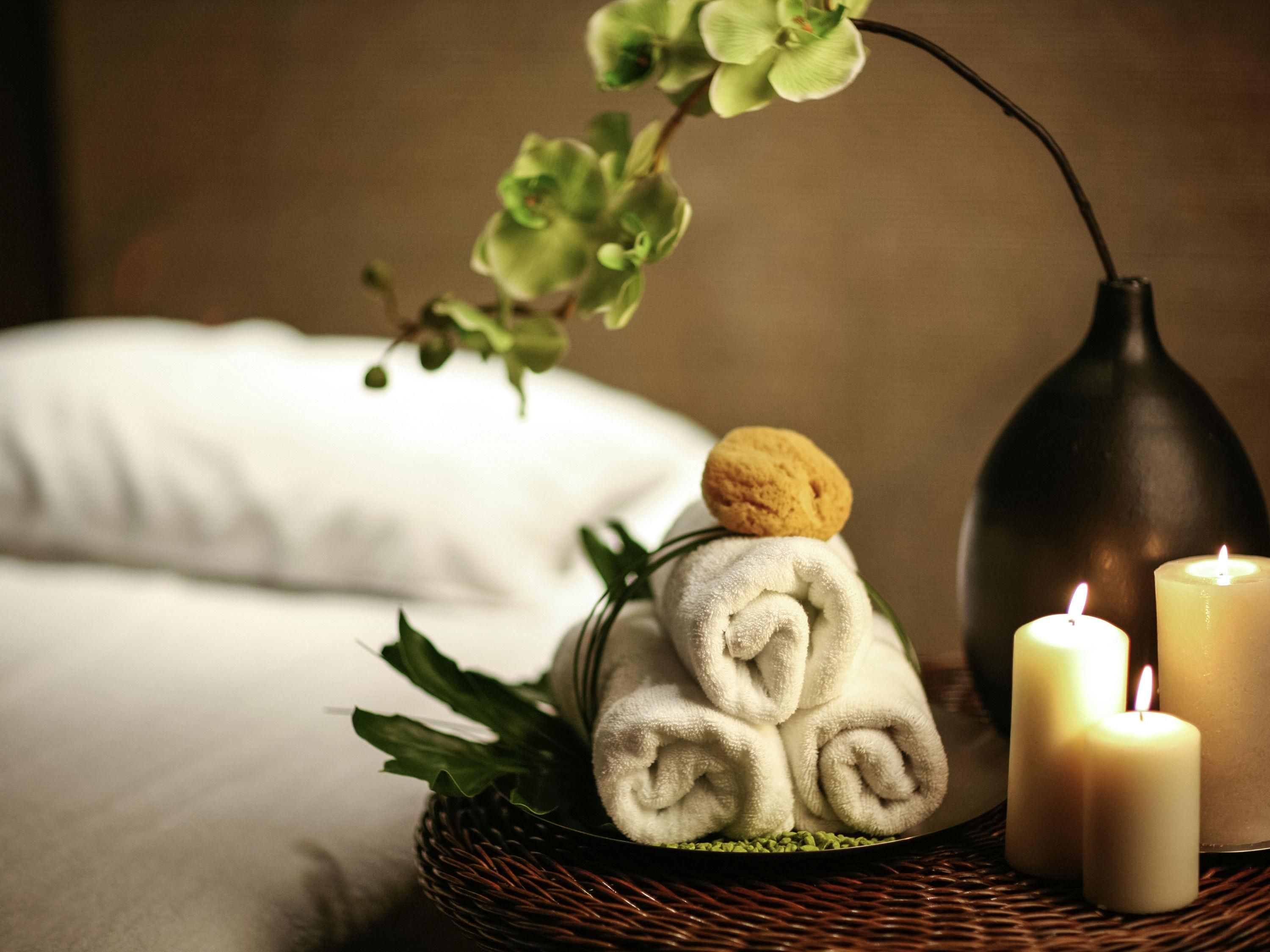 A wicker basket with rolled towels, a candle, and a plant.