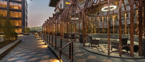 A modern building with a geometric tiled floor, a metal fence with circular patterns, and outdoor seating.