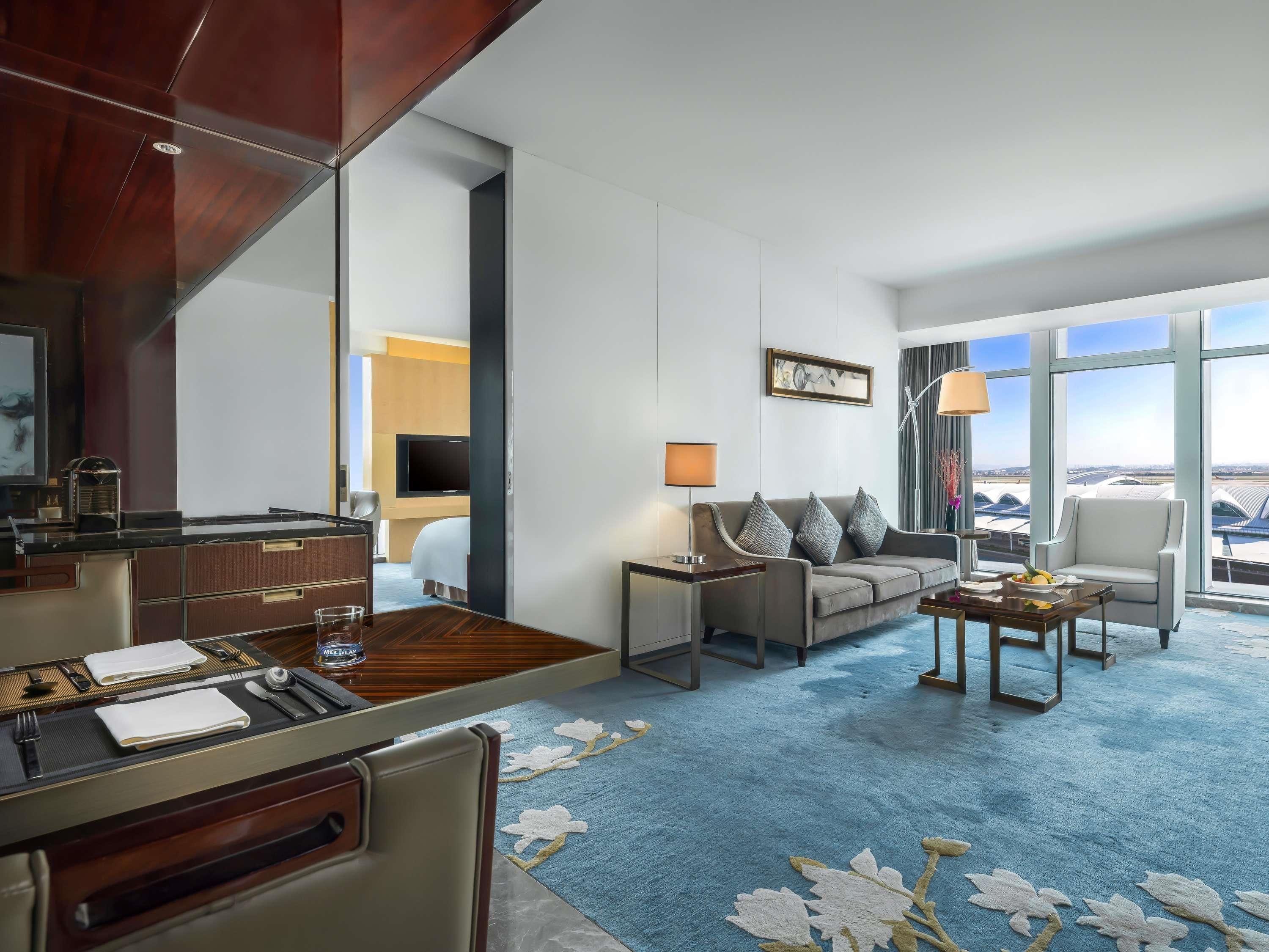 Une chambre d’hôtel avec un coin repas, un canapé, une télévision et une grande fenêtre donnant sur un beau paysage.