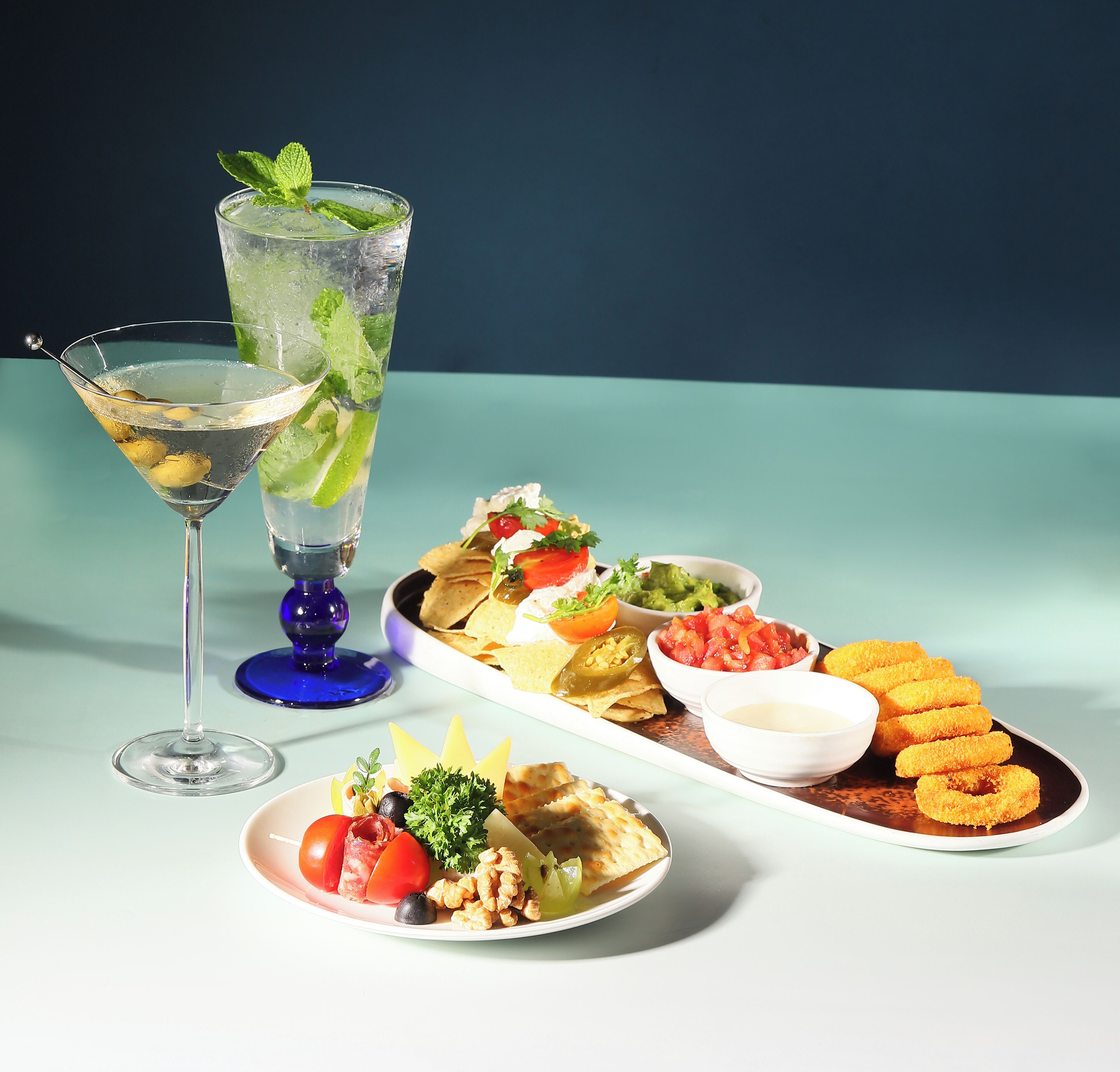 Una copa de martini y un vaso alto con una cuña de lima y hojas de menta.