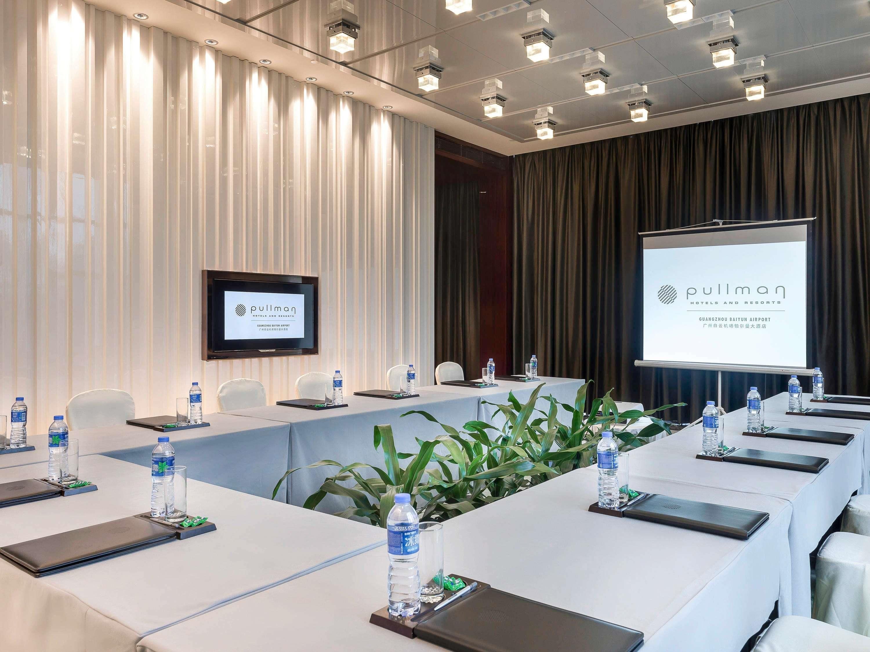 A conference room with a long table, chairs, water bottles, and a screen displaying the hotel name.