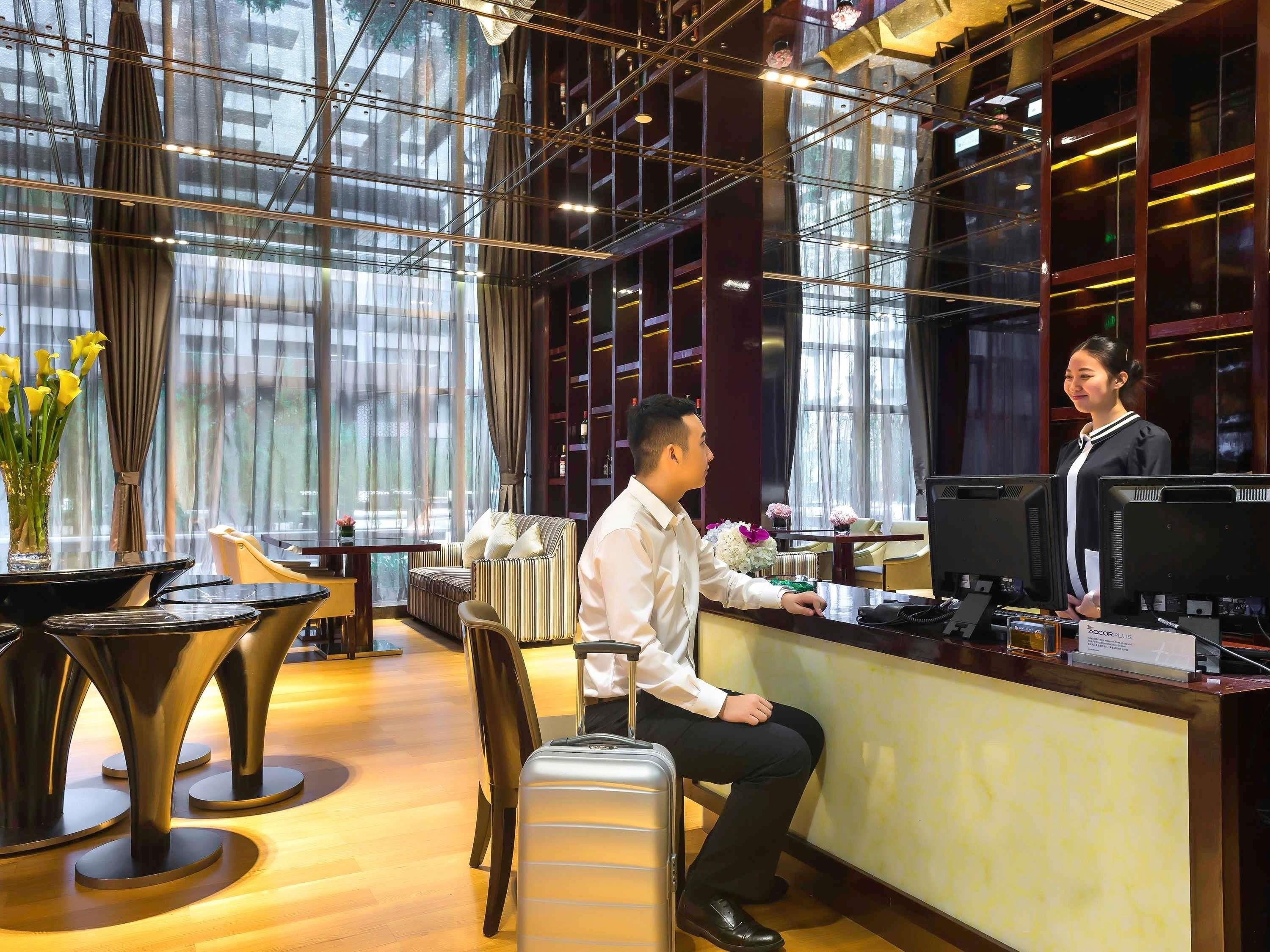 Un espace d’accueil d’hôtel au design moderne, comprenant un comptoir d’accueil, un coin salon et de grandes fenêtres.