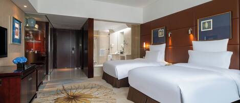 Habitación de hotel con dos camas, un escritorio, un tocador y un baño visible a través de una puerta abierta.